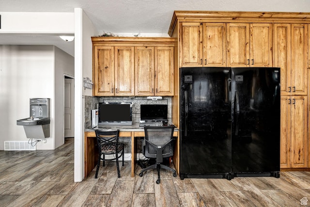 kitchen featuring tasteful backsplash, visible vents, wood tiled floor, freestanding refrigerator, and brown cabinetry