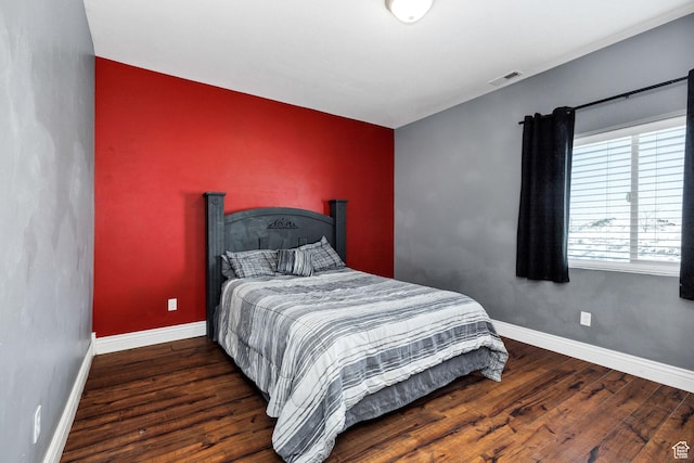 bedroom with an accent wall, wood finished floors, visible vents, and baseboards
