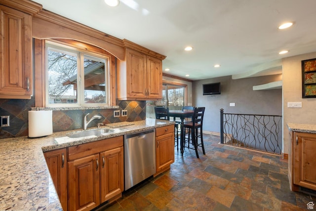 kitchen featuring baseboards, dishwasher, decorative backsplash, stone finish floor, and a sink