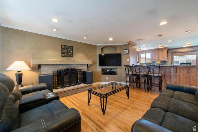 living room featuring recessed lighting, a fireplace with raised hearth, ornamental molding, and light wood finished floors