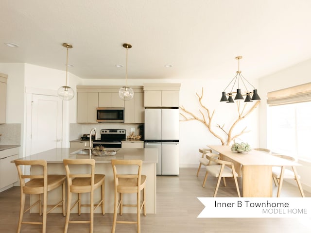 kitchen featuring light wood finished floors, backsplash, a breakfast bar area, an island with sink, and stainless steel appliances