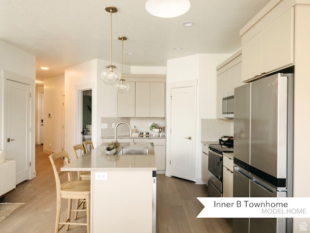 kitchen with a breakfast bar area, an island with sink, a sink, light wood-style floors, and appliances with stainless steel finishes