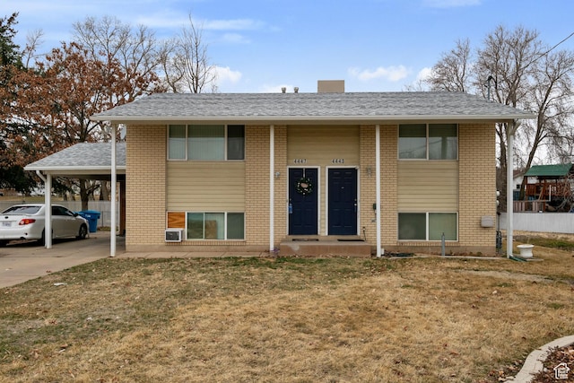 raised ranch with driveway, a front yard, a shingled roof, an attached carport, and brick siding