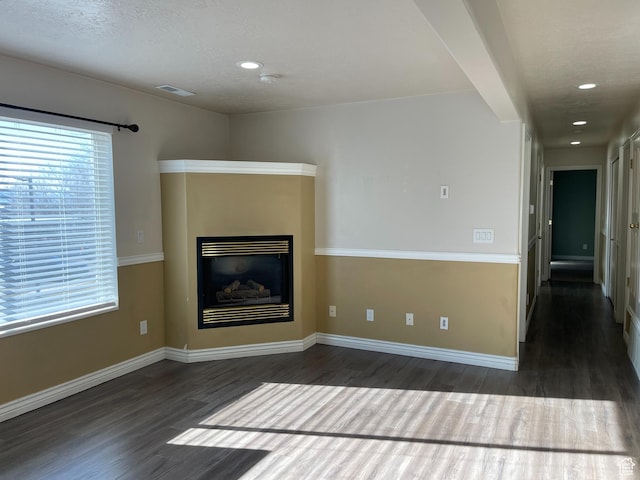 unfurnished living room with a glass covered fireplace, wood finished floors, visible vents, and baseboards