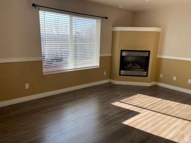 unfurnished living room featuring visible vents, wood finished floors, baseboards, and a glass covered fireplace