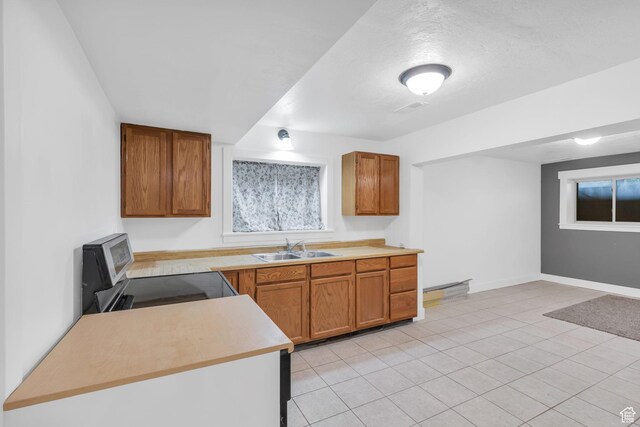 kitchen with brown cabinetry, electric range oven, light countertops, and a sink