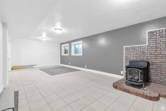 unfurnished living room with baseboards, a wood stove, a textured ceiling, and tile patterned flooring