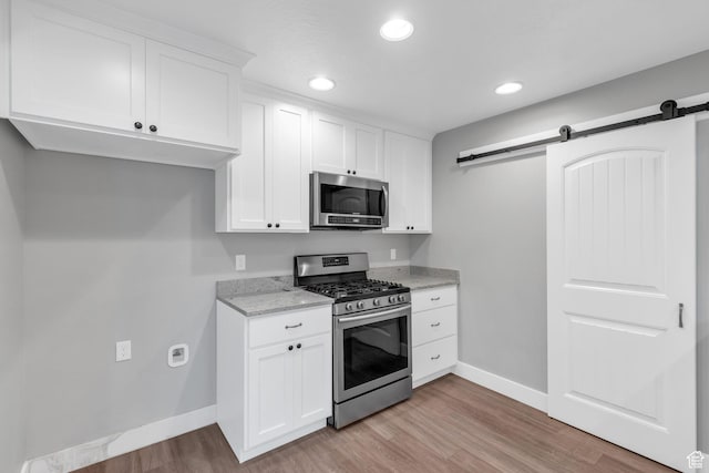 kitchen with appliances with stainless steel finishes, a barn door, baseboards, light stone countertops, and light wood finished floors