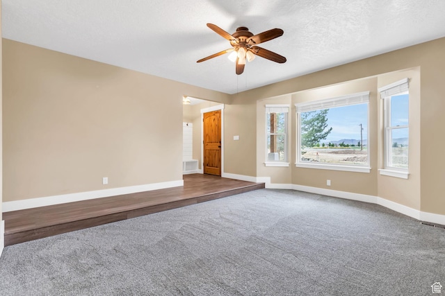 empty room with dark carpet, ceiling fan, visible vents, and baseboards