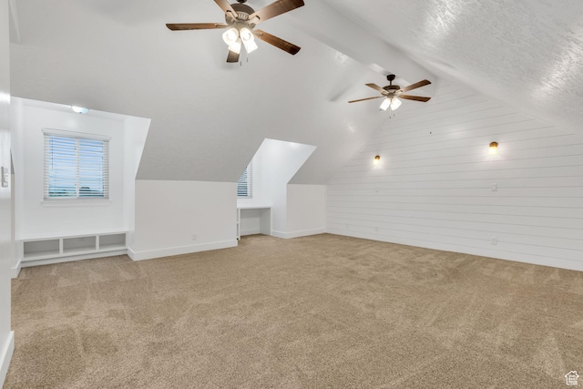 bonus room with wood walls, light colored carpet, ceiling fan, and lofted ceiling with beams