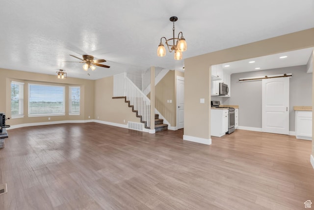 unfurnished living room featuring stairway, a barn door, light wood-type flooring, visible vents, and ceiling fan with notable chandelier