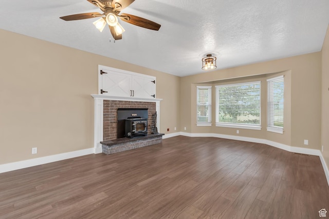 unfurnished living room with baseboards, dark wood-style floors, a wood stove, a ceiling fan, and a textured ceiling