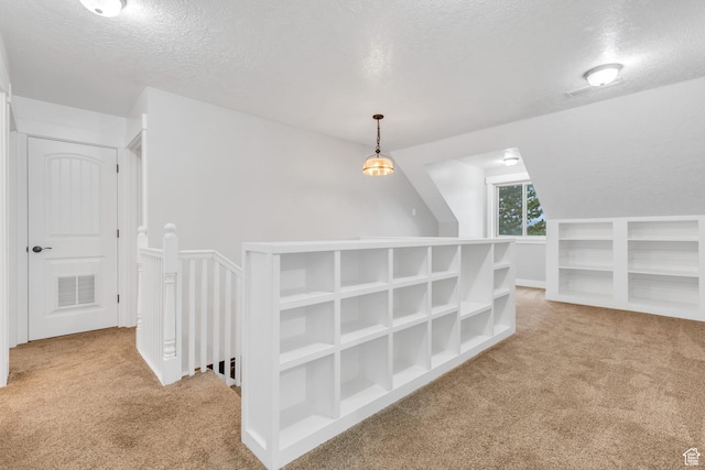 corridor featuring an upstairs landing, a textured ceiling, visible vents, and carpet floors