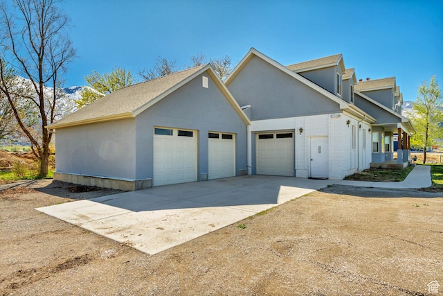 view of side of property featuring brick siding, stucco siding, a shingled roof, and an attached garage