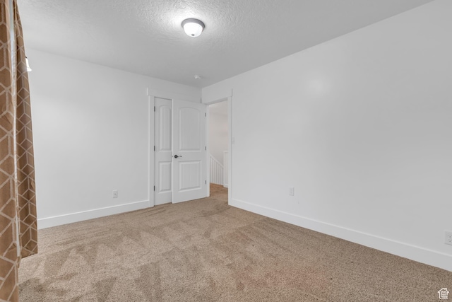 carpeted spare room with a textured ceiling and baseboards