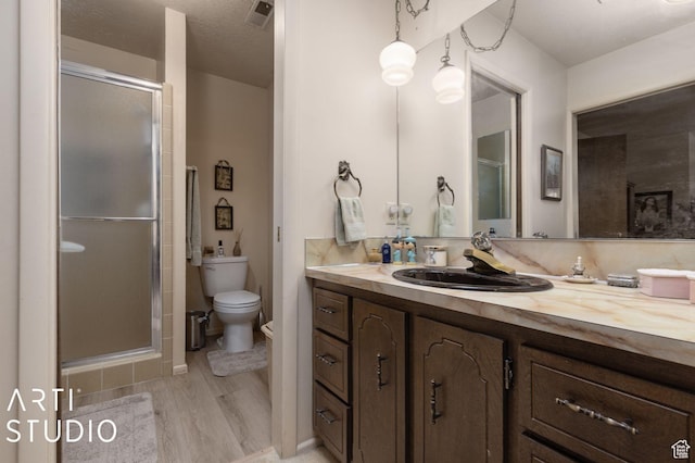 full bathroom with visible vents, toilet, wood finished floors, a shower stall, and vanity