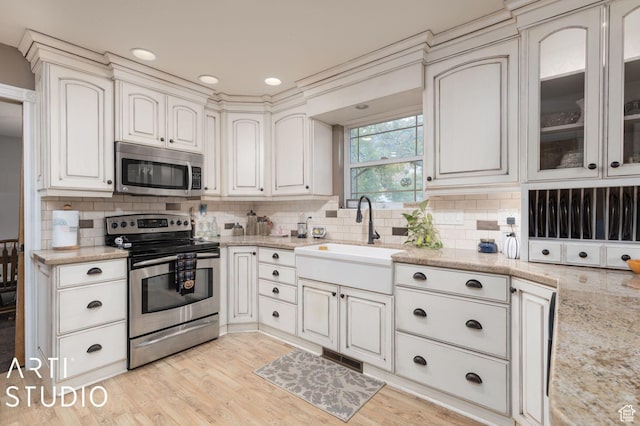 kitchen with light stone counters, light wood-style flooring, a sink, appliances with stainless steel finishes, and backsplash