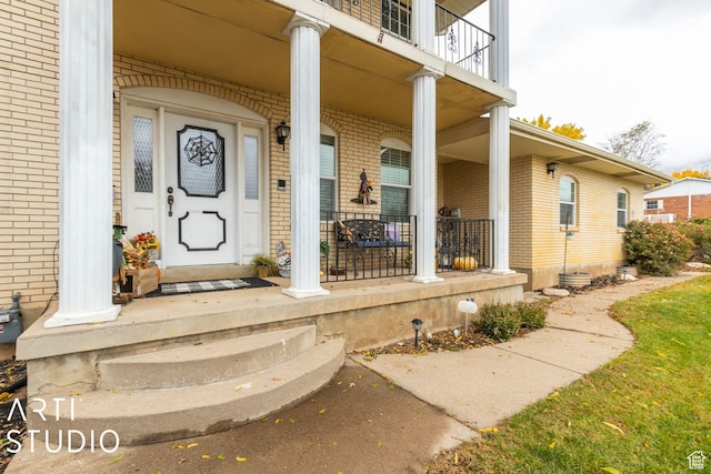 view of exterior entry with a porch, a balcony, and brick siding