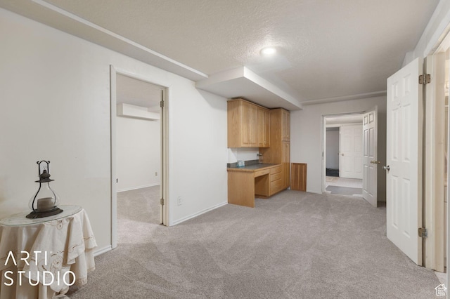 kitchen featuring an AC wall unit, light colored carpet, baseboards, and a textured ceiling