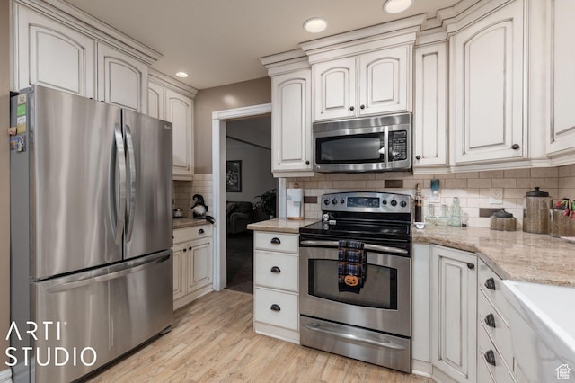 kitchen featuring light stone countertops, light wood-style flooring, stainless steel appliances, decorative backsplash, and cream cabinetry