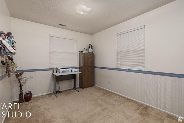 unfurnished office featuring visible vents, a wainscoted wall, carpet floors, and a textured ceiling