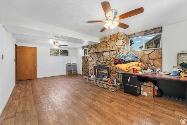 living area featuring a ceiling fan, a textured ceiling, wood finished floors, a fireplace, and baseboards