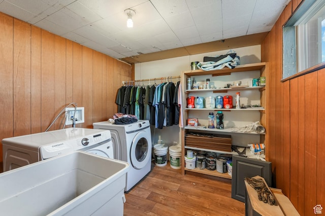 laundry area featuring wood finished floors, laundry area, separate washer and dryer, a sink, and wood walls