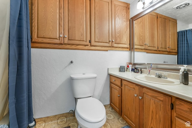 full bathroom with visible vents, toilet, vanity, and a textured wall