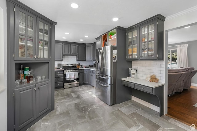 kitchen featuring gray cabinets, light countertops, glass insert cabinets, appliances with stainless steel finishes, and backsplash