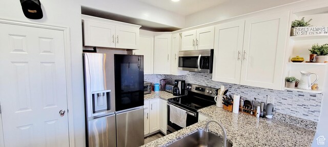 kitchen featuring backsplash, appliances with stainless steel finishes, white cabinetry, and light stone countertops