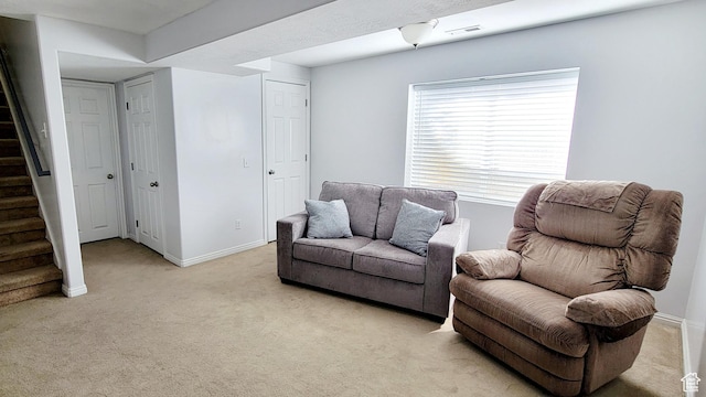 living area featuring stairway, baseboards, and light colored carpet