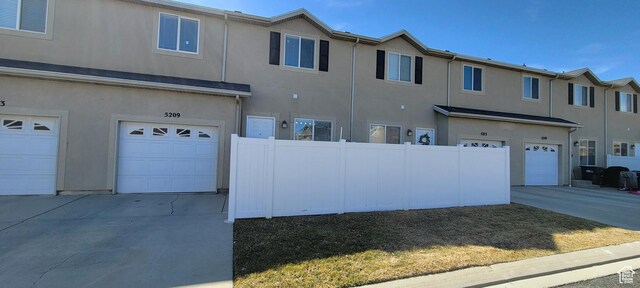 view of front facade with stucco siding, an attached garage, driveway, and fence