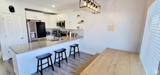 kitchen with light stone counters, a peninsula, a sink, decorative backsplash, and stainless steel appliances