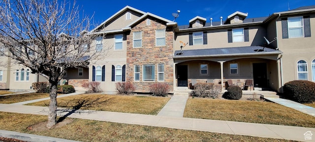 view of property featuring a porch, a front lawn, stone siding, and stucco siding