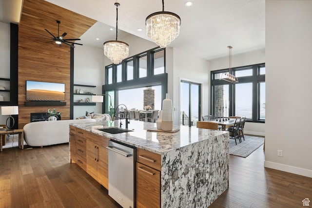 kitchen with brown cabinetry, dark wood finished floors, dishwasher, ceiling fan with notable chandelier, and a sink