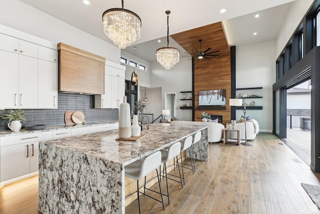 kitchen featuring a large island with sink, decorative backsplash, light wood-type flooring, and white cabinets