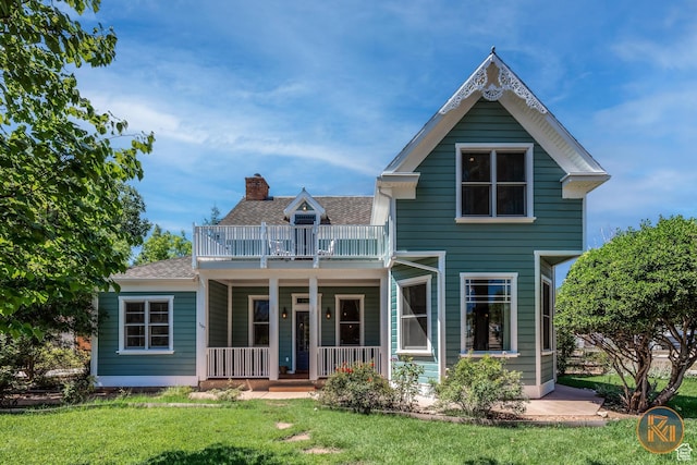 view of front of house with a front yard, a balcony, covered porch, a chimney, and a shingled roof