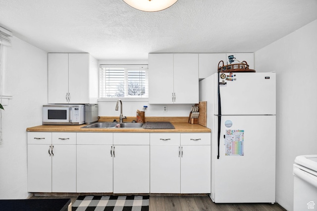 kitchen featuring light countertops, wood finished floors, white appliances, white cabinetry, and a sink
