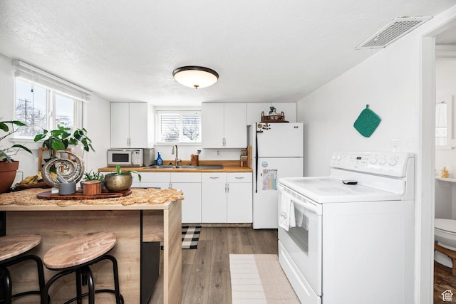 kitchen featuring a wealth of natural light, visible vents, white appliances, and a sink