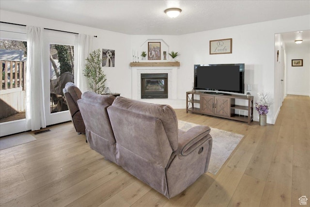 living room featuring visible vents, baseboards, a glass covered fireplace, and light wood finished floors