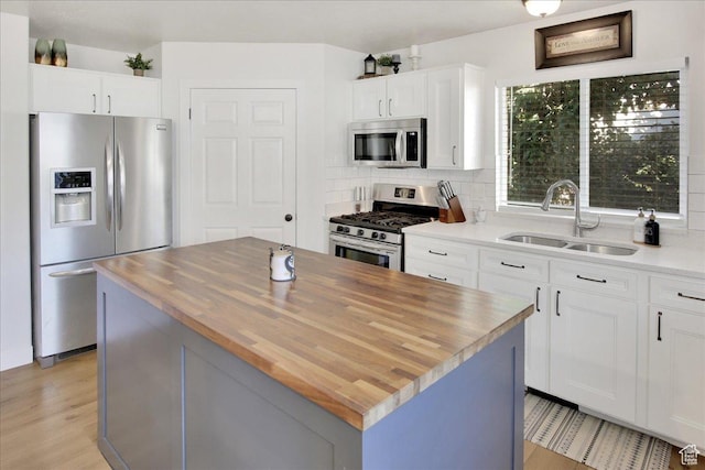 kitchen featuring backsplash, wooden counters, white cabinets, stainless steel appliances, and a sink