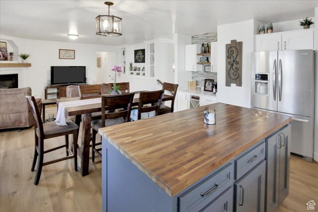 kitchen with a glass covered fireplace, stainless steel fridge, white cabinets, and wood counters