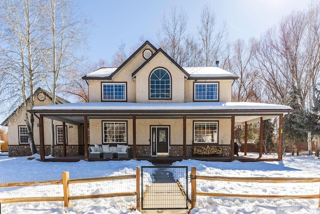view of front of house with a gate, covered porch, stucco siding, stone siding, and a fenced front yard