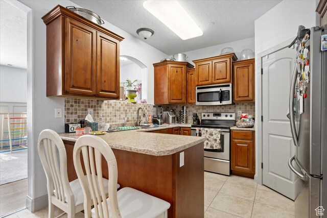 3635 E Clear Rock Rd Unit 4, Eagle Mountain, UT 84005 - kitchen with tasteful backsplash, appliances with stainless steel finishes, a peninsula, brown cabinetry, and a sink