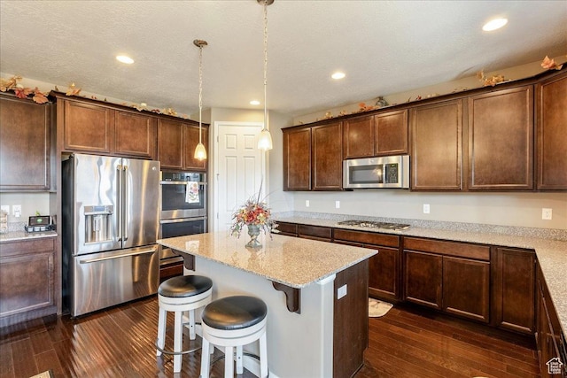 5663 W Yukon Park Ln S, Herriman, UT 84096 - kitchen featuring appliances with stainless steel finishes, dark wood-type flooring, a kitchen island, light stone countertops, and a breakfast bar