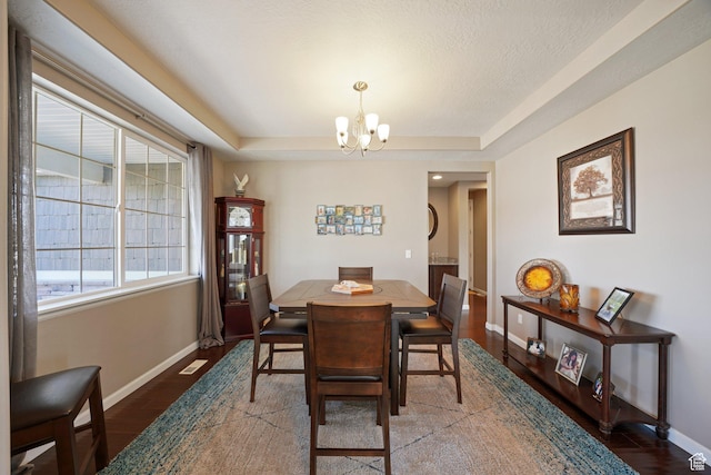 dining space featuring baseboards, an inviting chandelier, visible vents, a raised ceiling, and wood finished floors