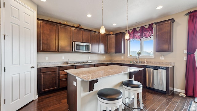 kitchen with a center island, a sink, appliances with stainless steel finishes, dark wood-style floors, and light stone counters