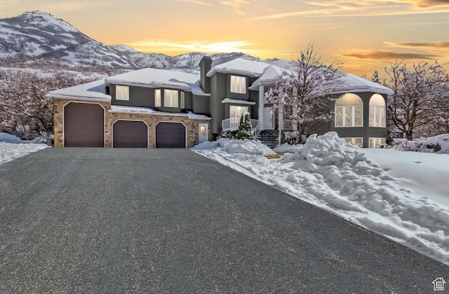 view of front of home with gravel driveway, a mountain view, stone siding, and a chimney