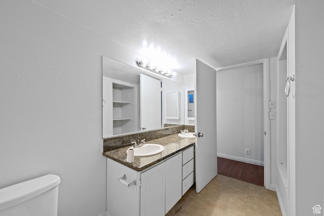 bathroom featuring double vanity, a sink, tile patterned flooring, a textured ceiling, and toilet
