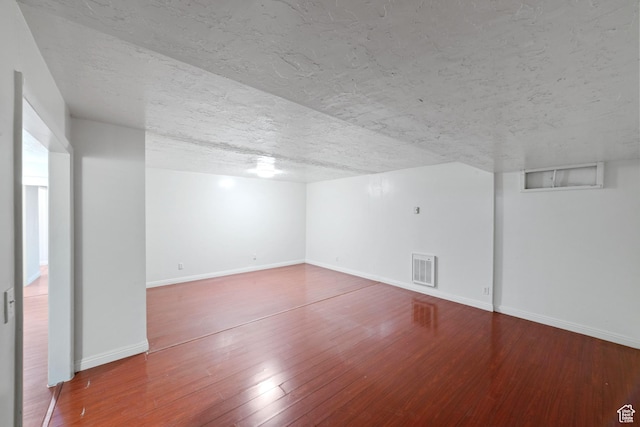 basement featuring hardwood / wood-style floors, baseboards, visible vents, and a textured ceiling